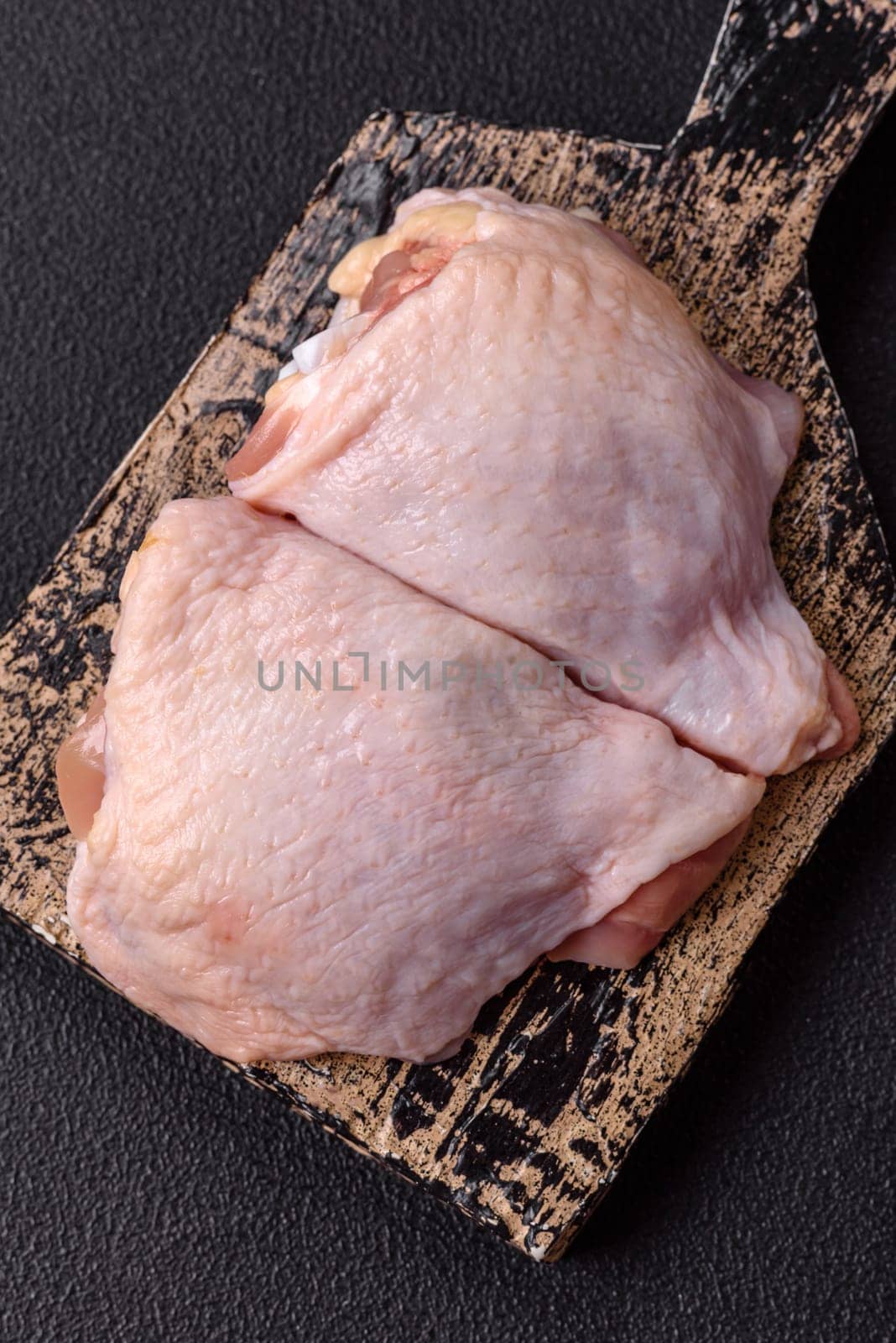 Fresh raw chicken thighs with salt and spices on dark concrete background