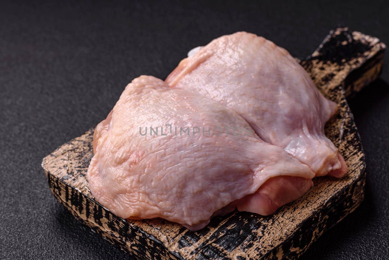 Fresh raw chicken thighs with salt and spices on dark concrete background