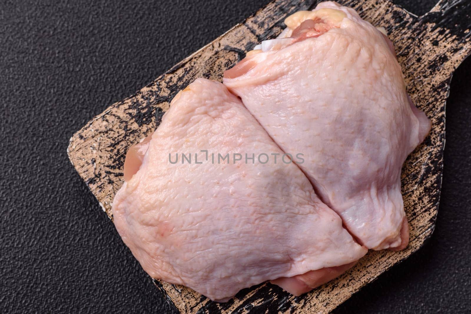 Fresh raw chicken thighs with salt and spices on dark concrete background