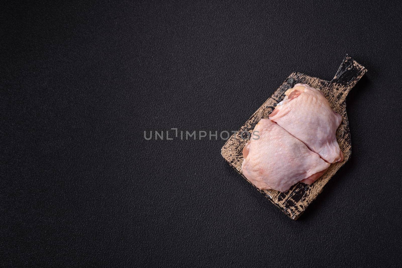 Fresh raw chicken thighs with salt and spices on dark concrete background