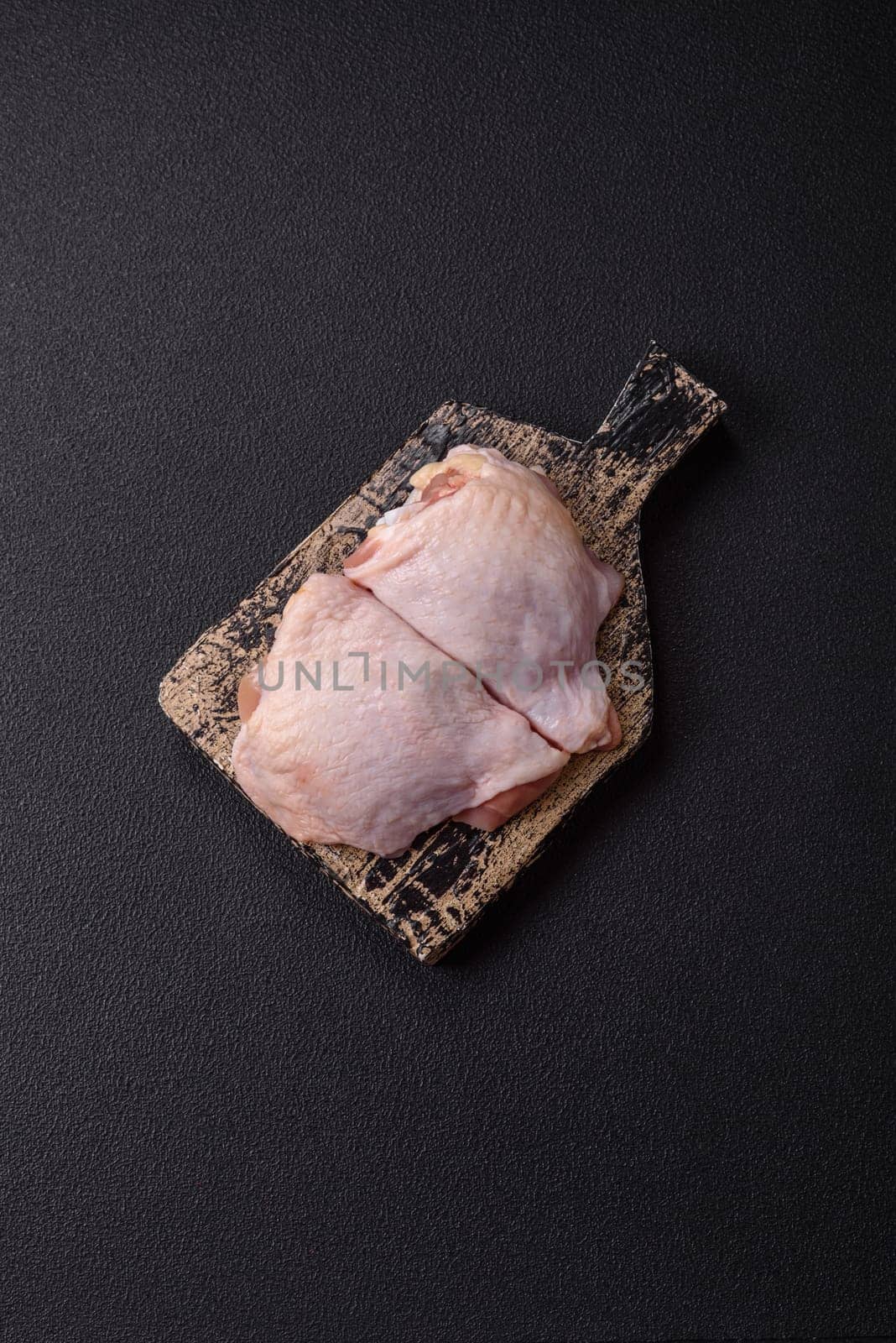 Fresh raw chicken thighs with salt and spices on dark concrete background