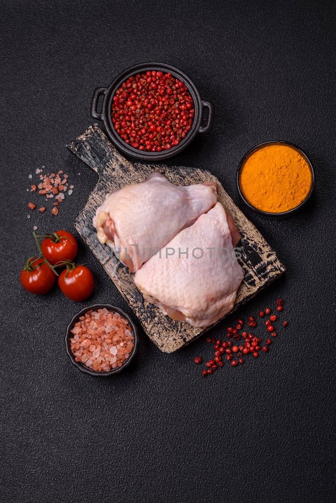 Fresh raw chicken thighs with salt and spices on dark concrete background