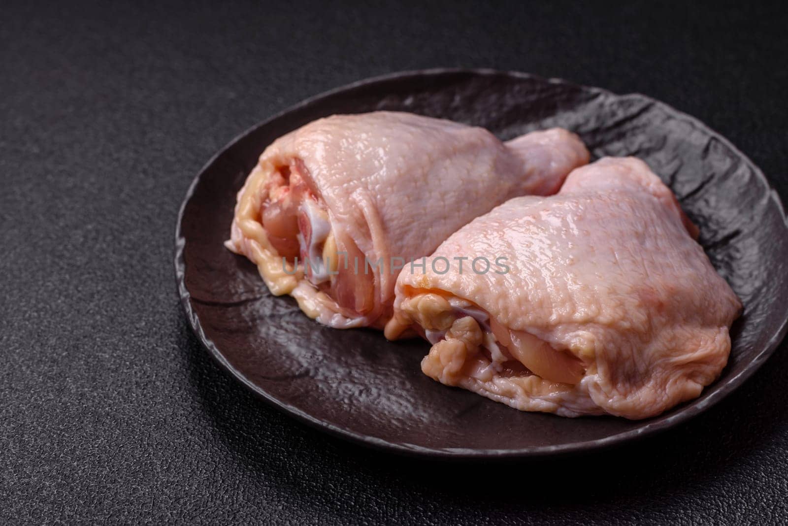 Fresh raw chicken thighs with salt and spices on dark concrete background
