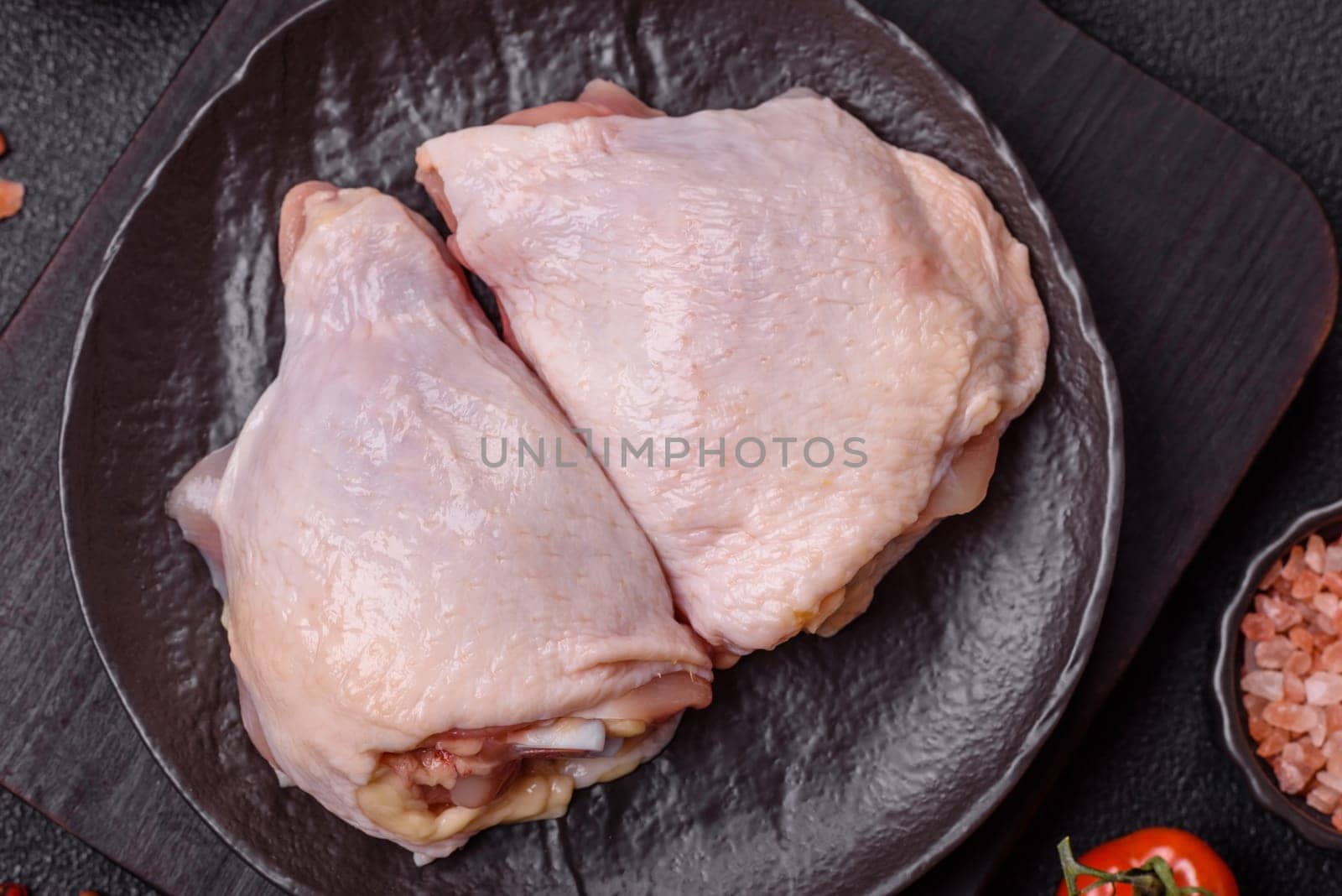 Fresh raw chicken thighs with salt and spices on dark concrete background