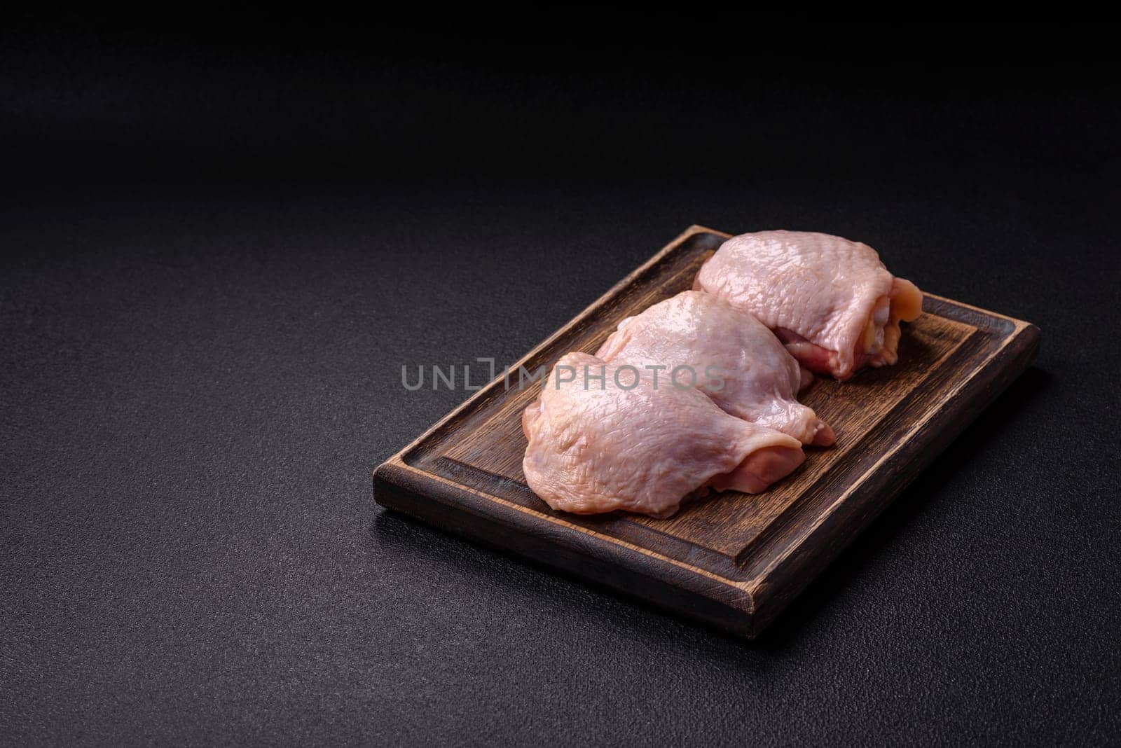 Fresh raw chicken thighs with salt and spices on dark concrete background