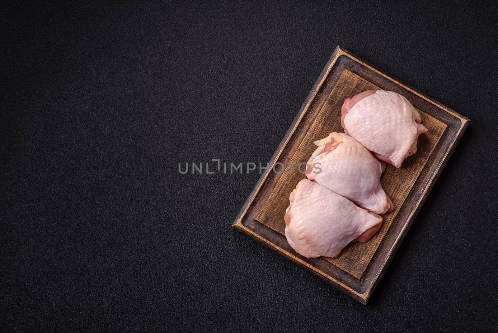 Fresh raw chicken thighs with salt and spices on dark concrete background