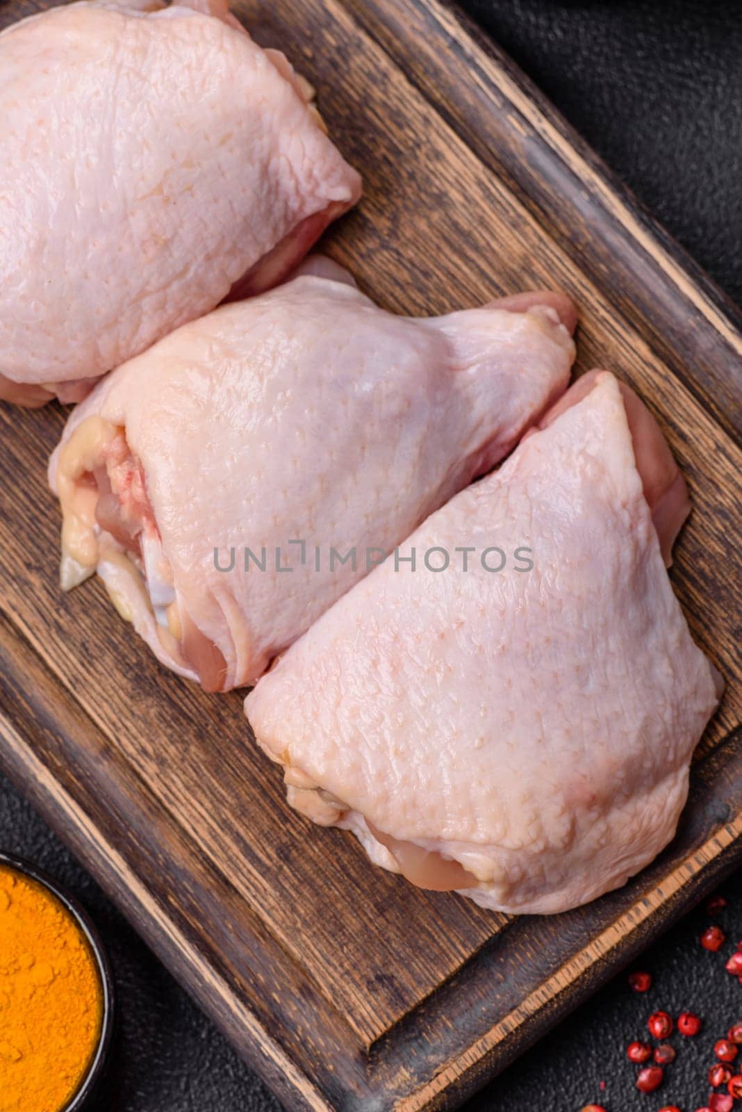 Fresh raw chicken thighs with salt and spices on dark concrete background