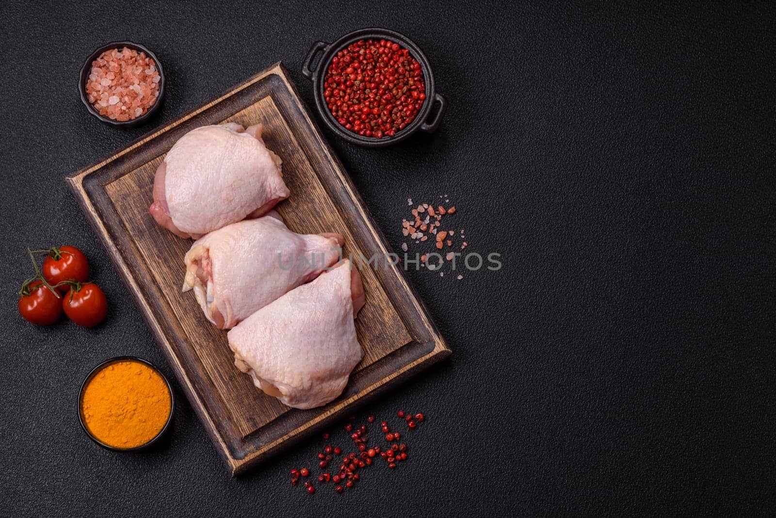 Fresh raw chicken thighs with salt and spices on dark concrete background