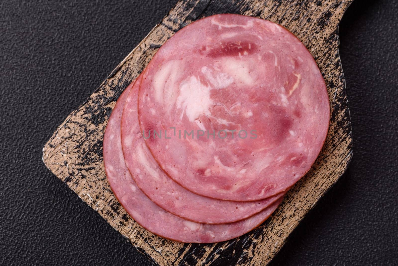 Boiled ham with salt and spices cut into slices on dark concrete background