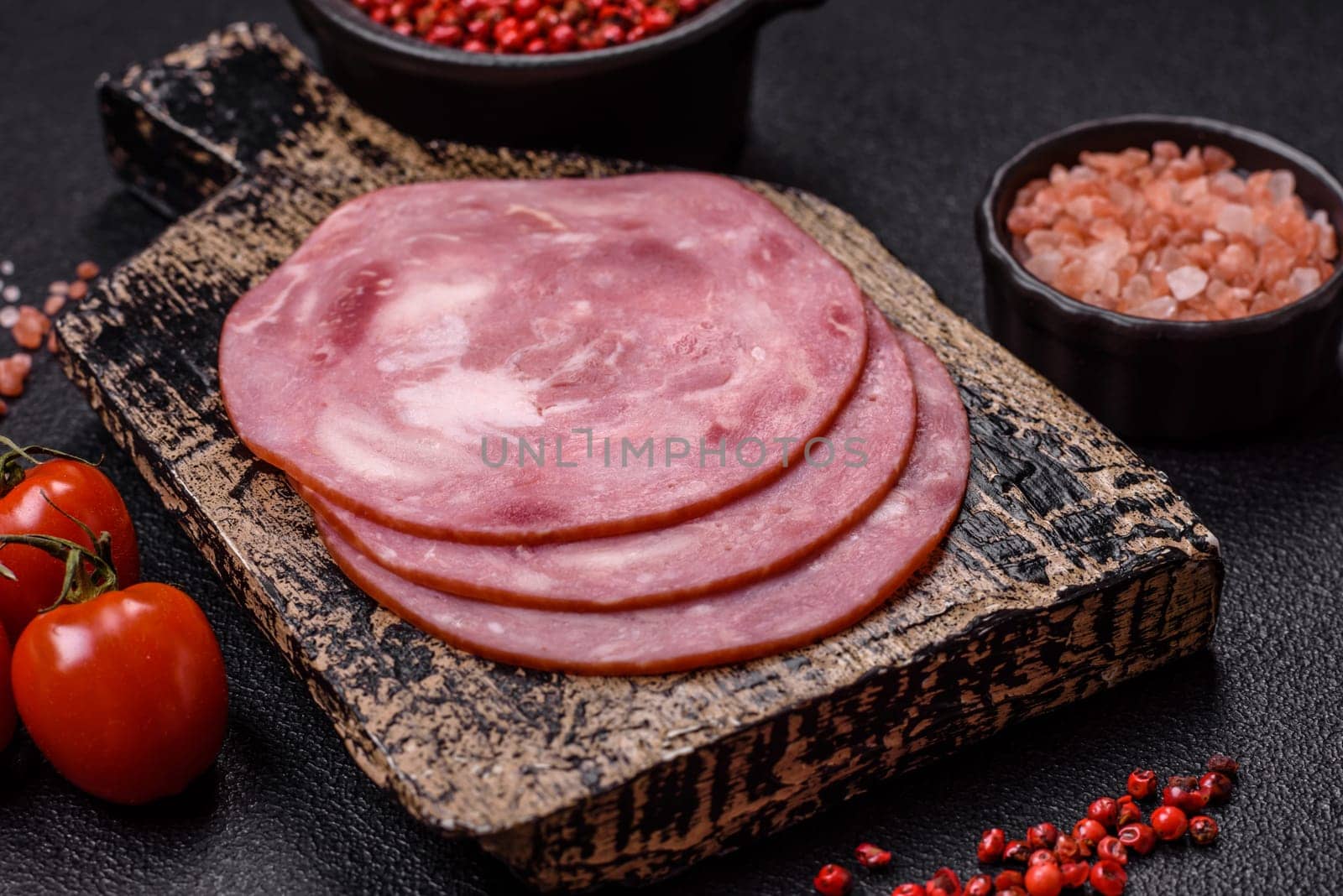 Boiled ham with salt and spices cut into slices on dark concrete background