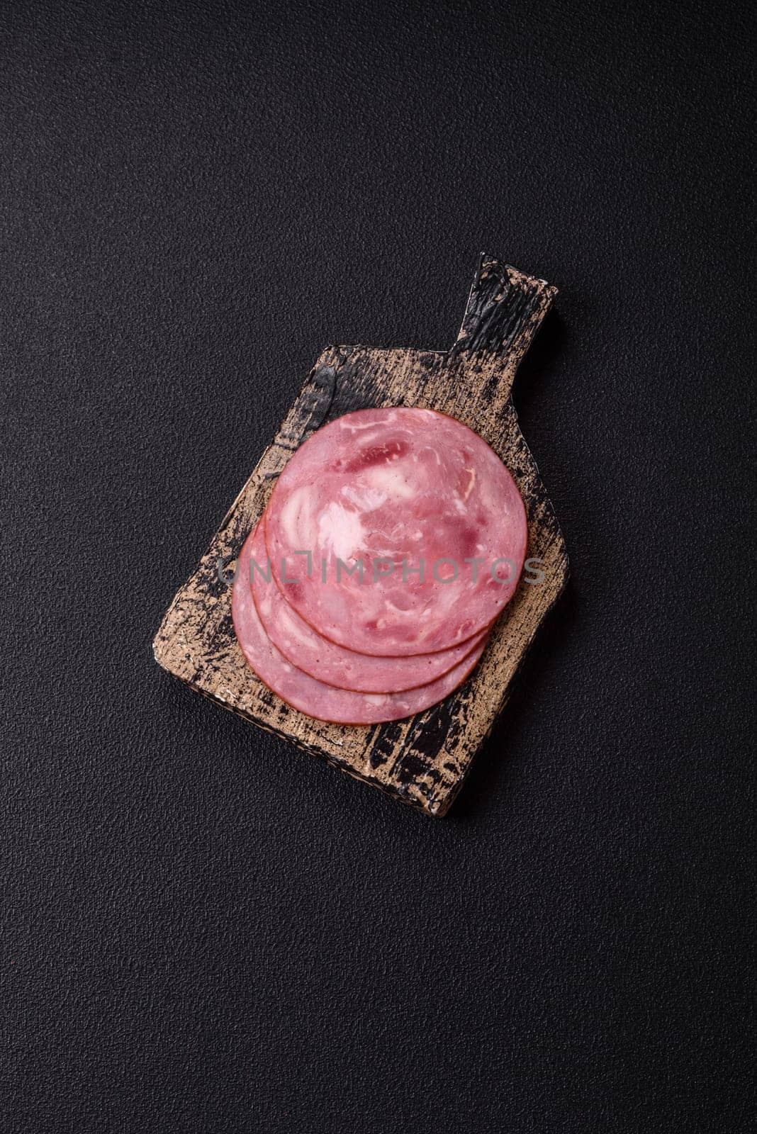 Boiled ham with salt and spices cut into slices on dark concrete background
