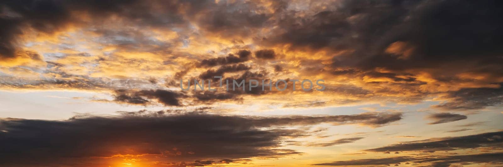 orange sunset in a cloudy sky with clouds at sunset in evening. Panoramic background with sky