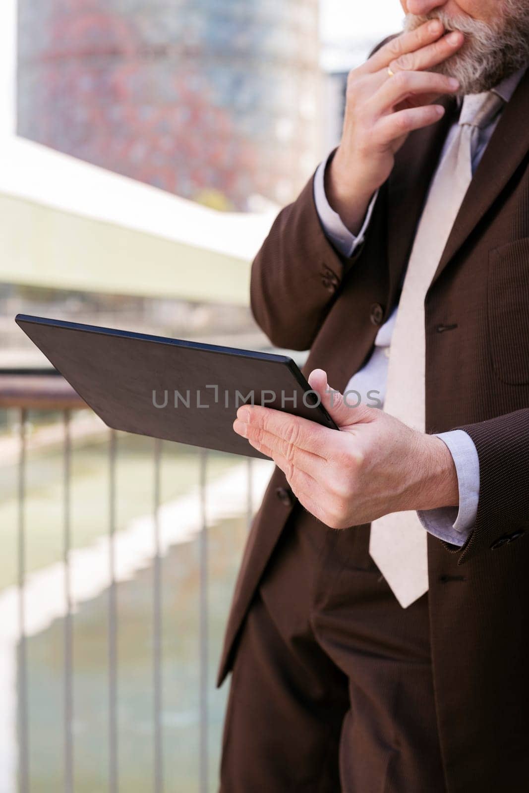 close up of a pensive unrecognizable man in formal outfit browsing tablet while standing at city, concept of technology of communication and business lifestyle