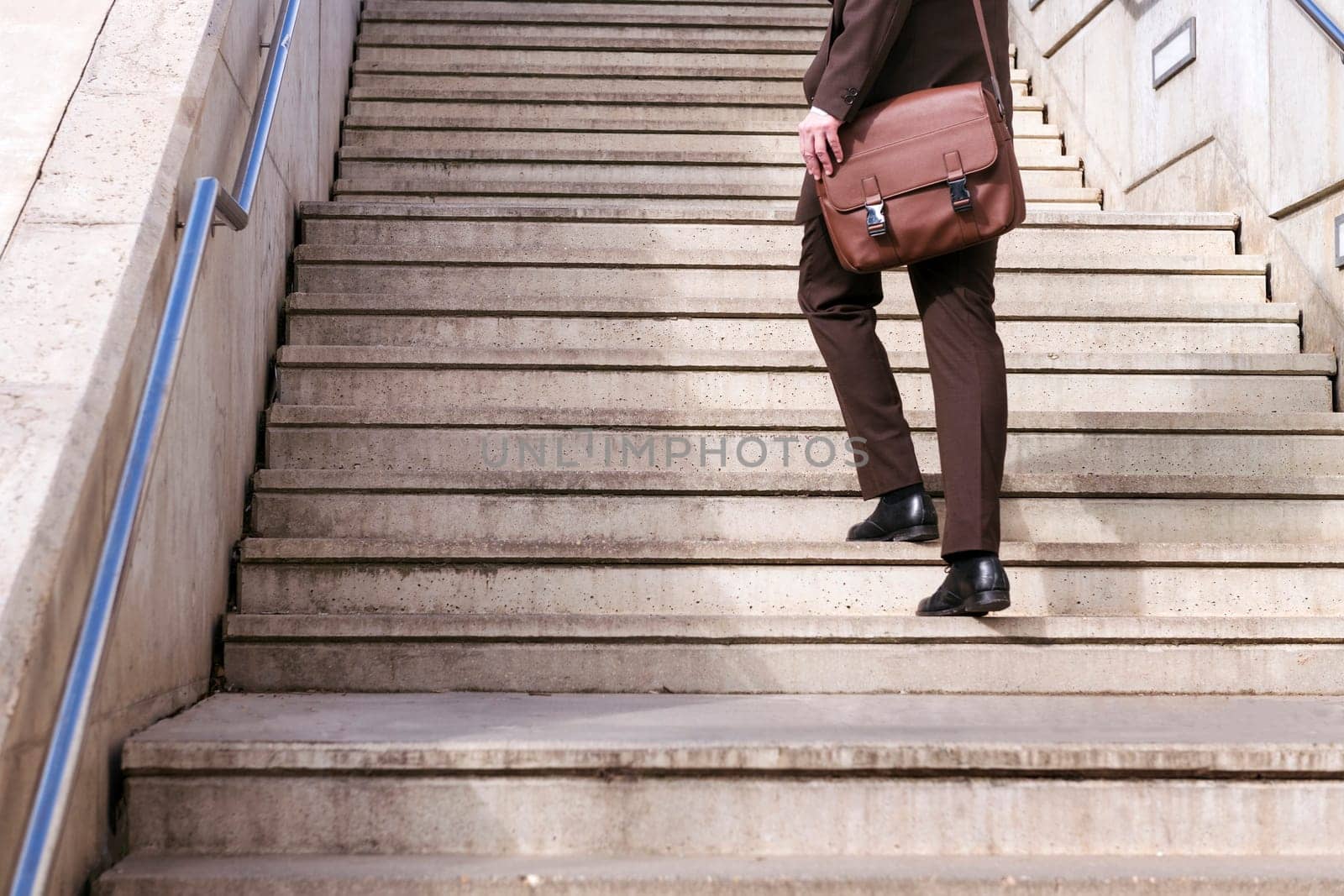 crop of the legs of unrecognizable stylish mature businessman in classy suit with briefcase walking up urban stairs in city, concept of business and middle age man lifestyle, copyspace for text