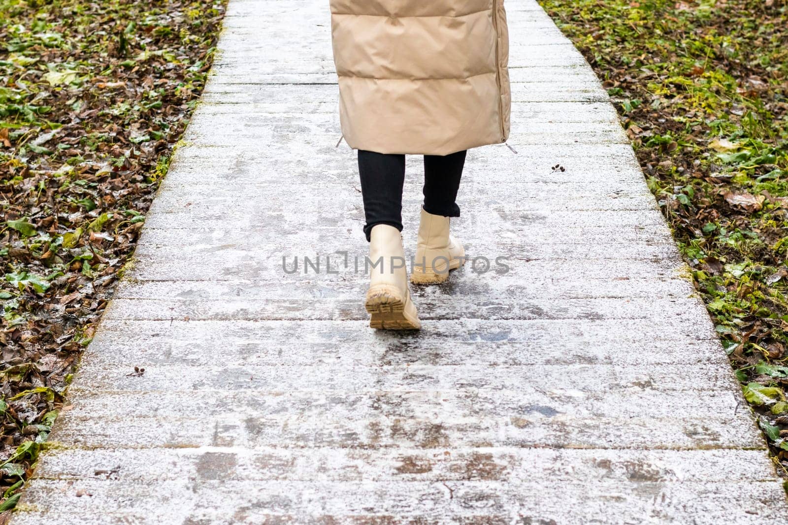 Woman walks on the wooden path walk in the park covered with frost