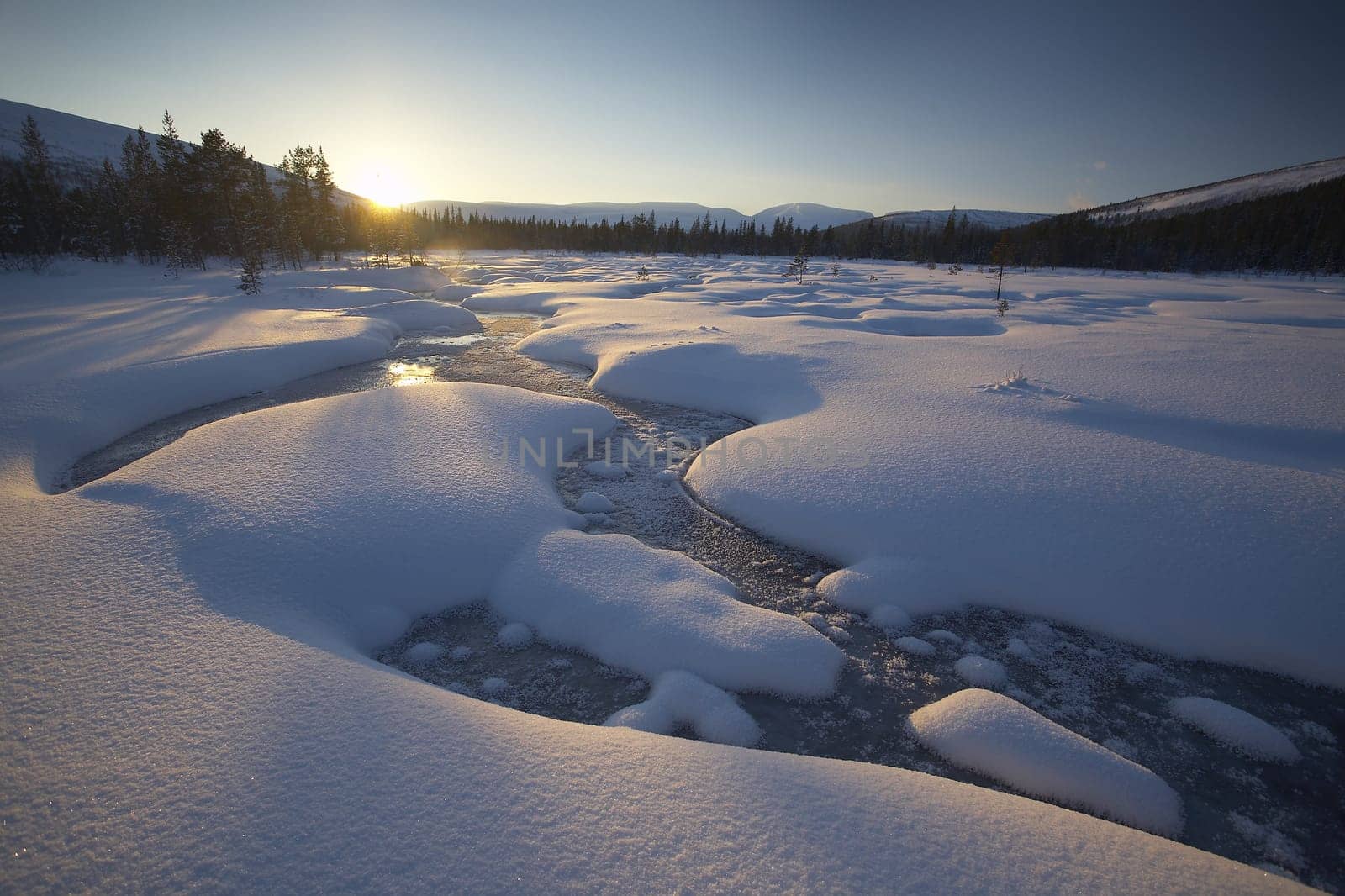 beautiful arctic winter landscape with snowy forest in the background, blue sky and sun setting on the horizon. cold climate
