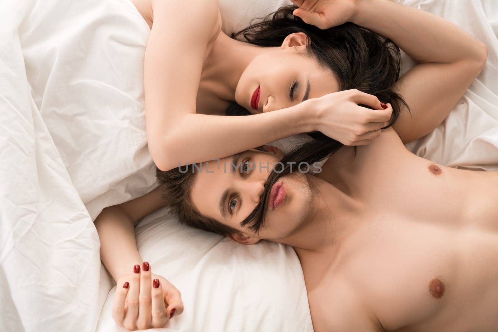 Loving couple in bed on white linen high angle cropped view