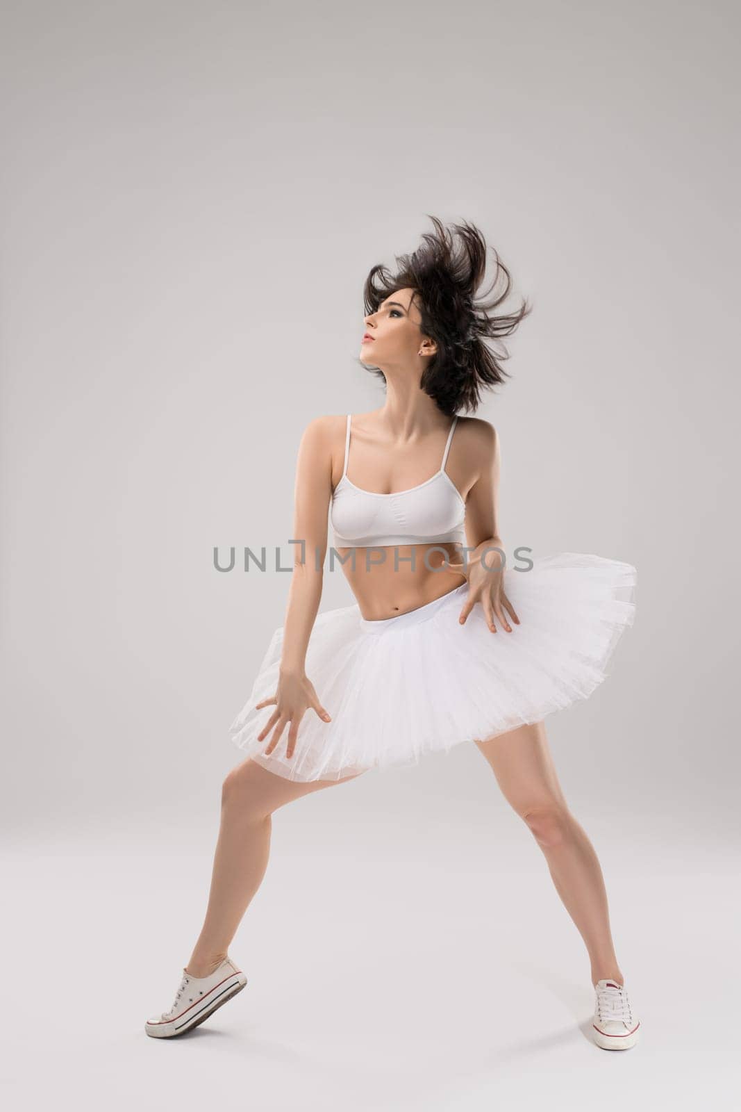 Beautiful charming ballerina in white suit posing on grey background