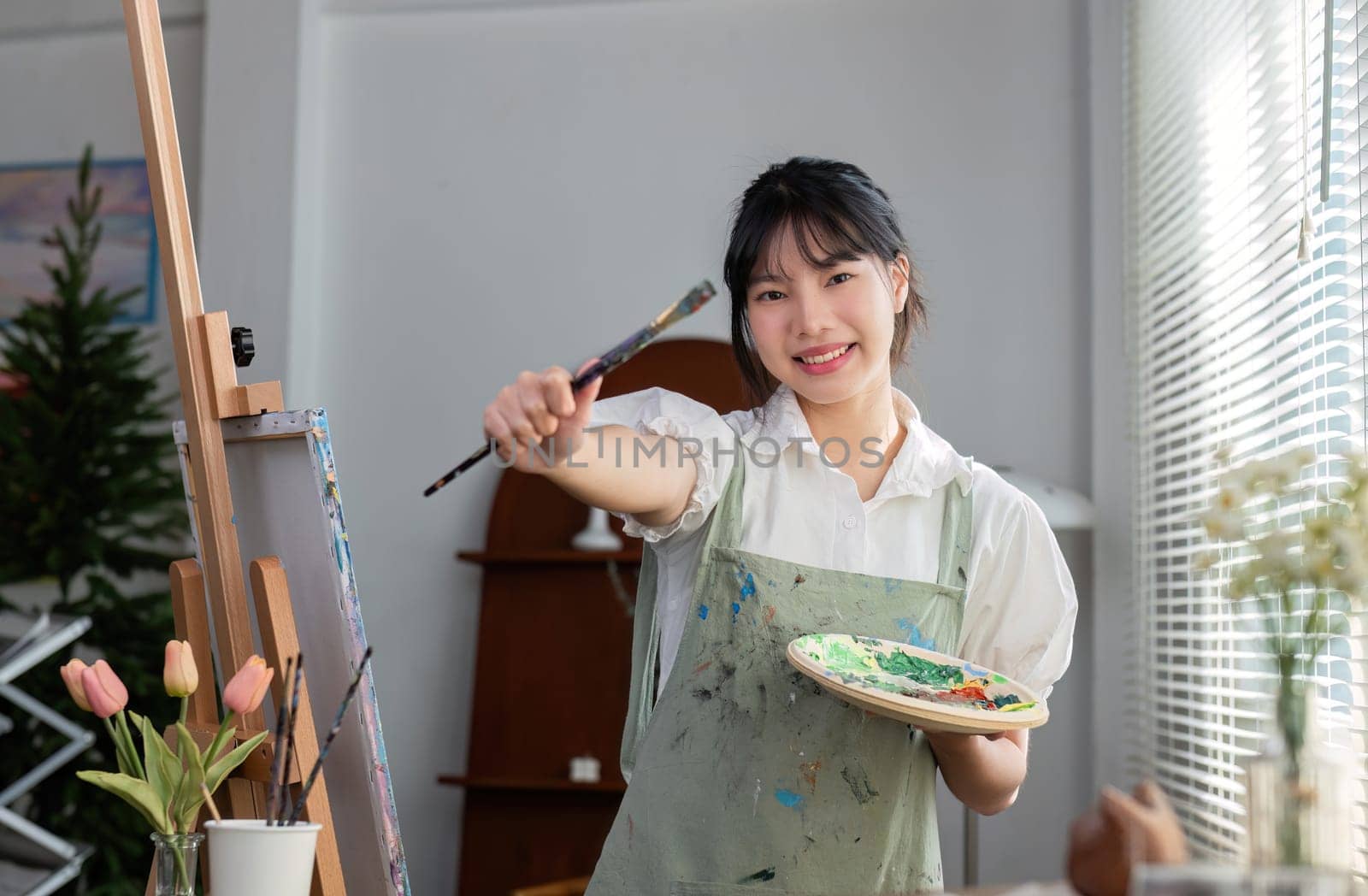 Portrait of a young female artist working on an abstract acrylic canvas painting in an art painting studio..