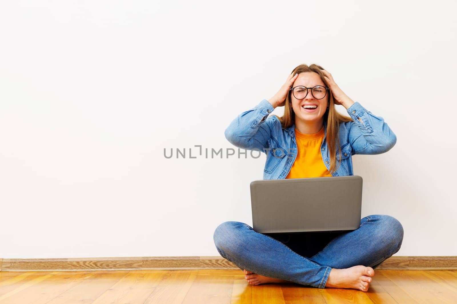 Stressed woman with laptop sitting on floor against white wall holding her head by andreyz