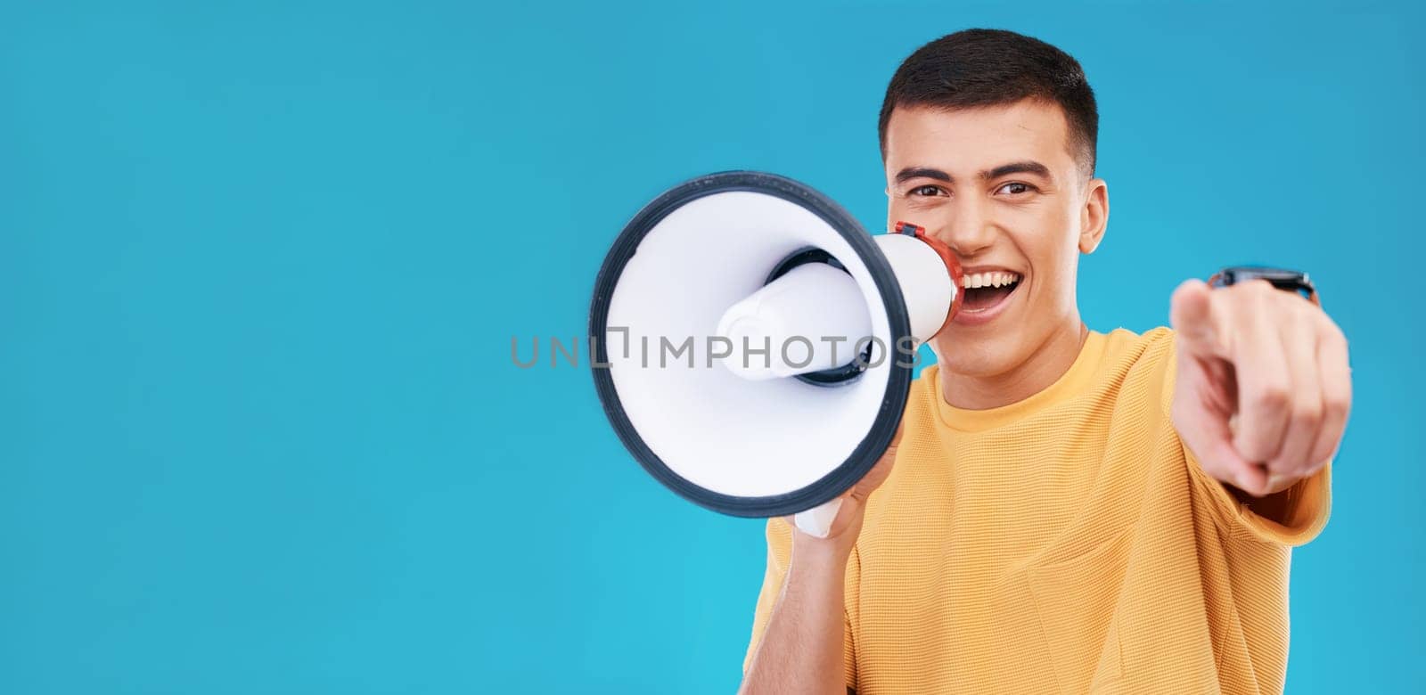 Megaphone, smile and portrait of man in studio pointing for announcement, speech or rally. Happy, protest and young person from Canada with bullhorn for loud communication isolated by blue background.