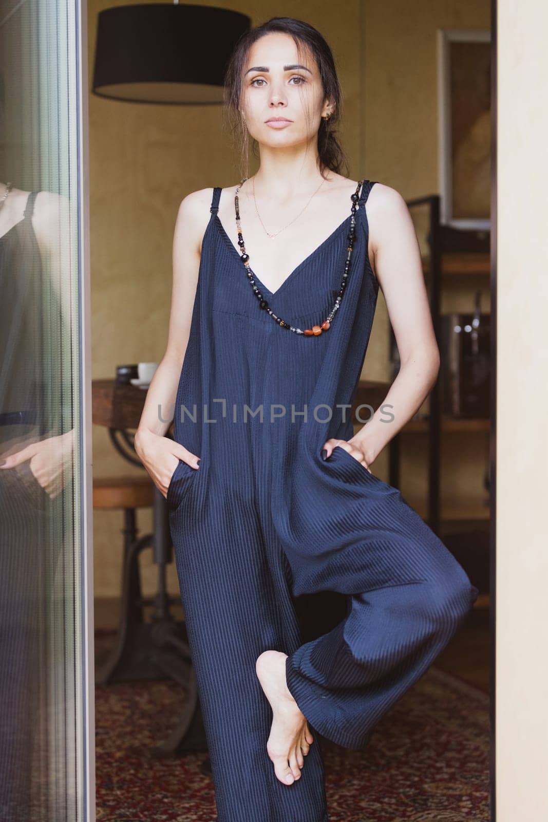 Summer fashion conception: Fashionable woman wearing jumpsuit, posing in stylish boho interior