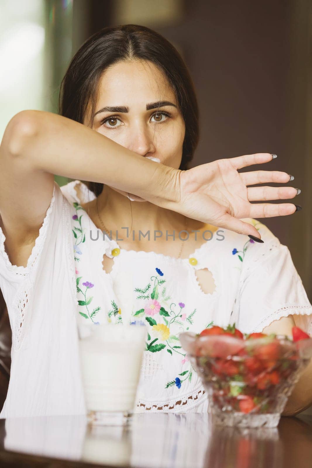 Portrait of a beautiful young woman dousing with cream. Artistic image of a young female with white fluid dripping. White liquid dripping into woman's mouth on light background. Erotic concept