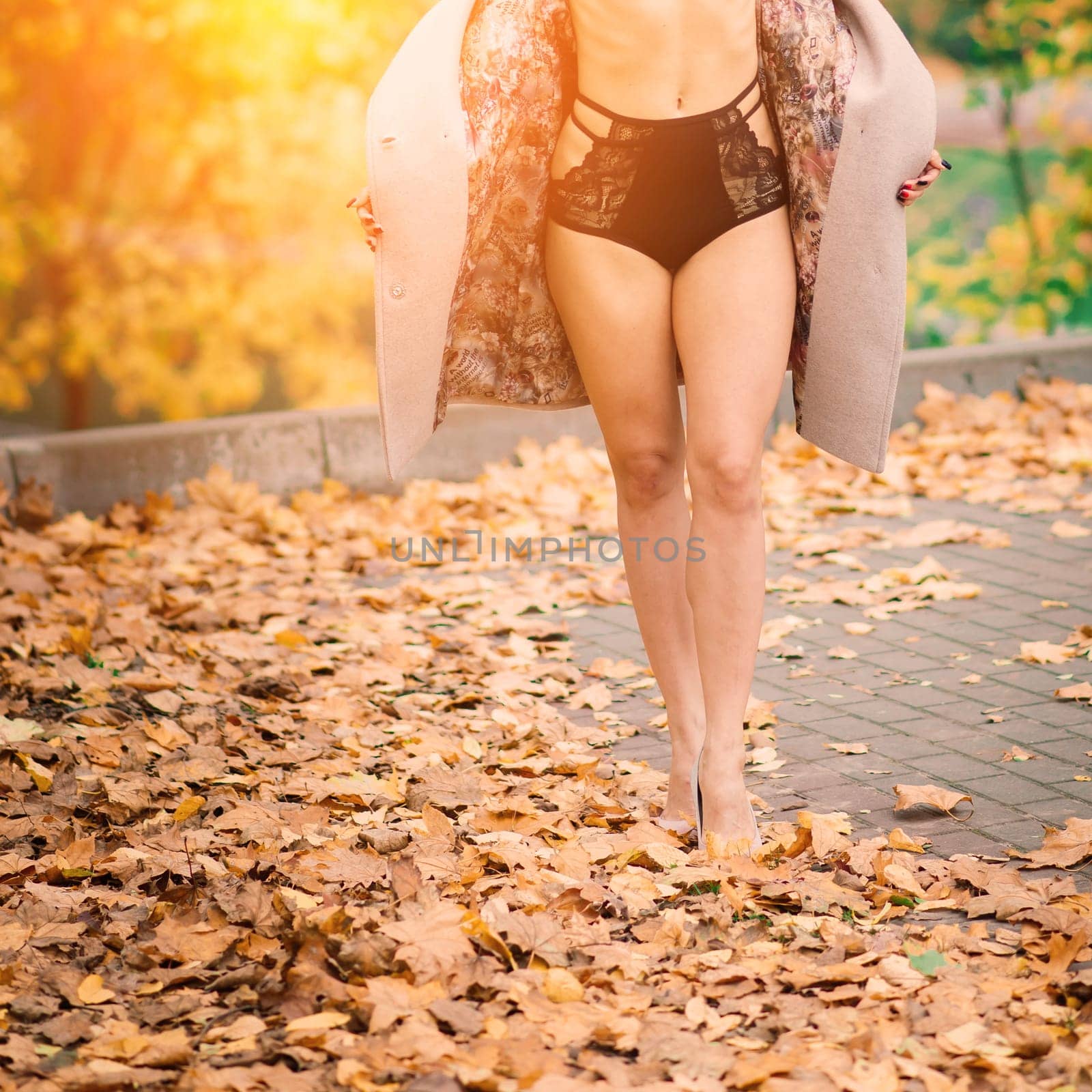 Young beautiful dark-haired woman with slender figure in lingerie and classic coat in autumn park by Zelenin