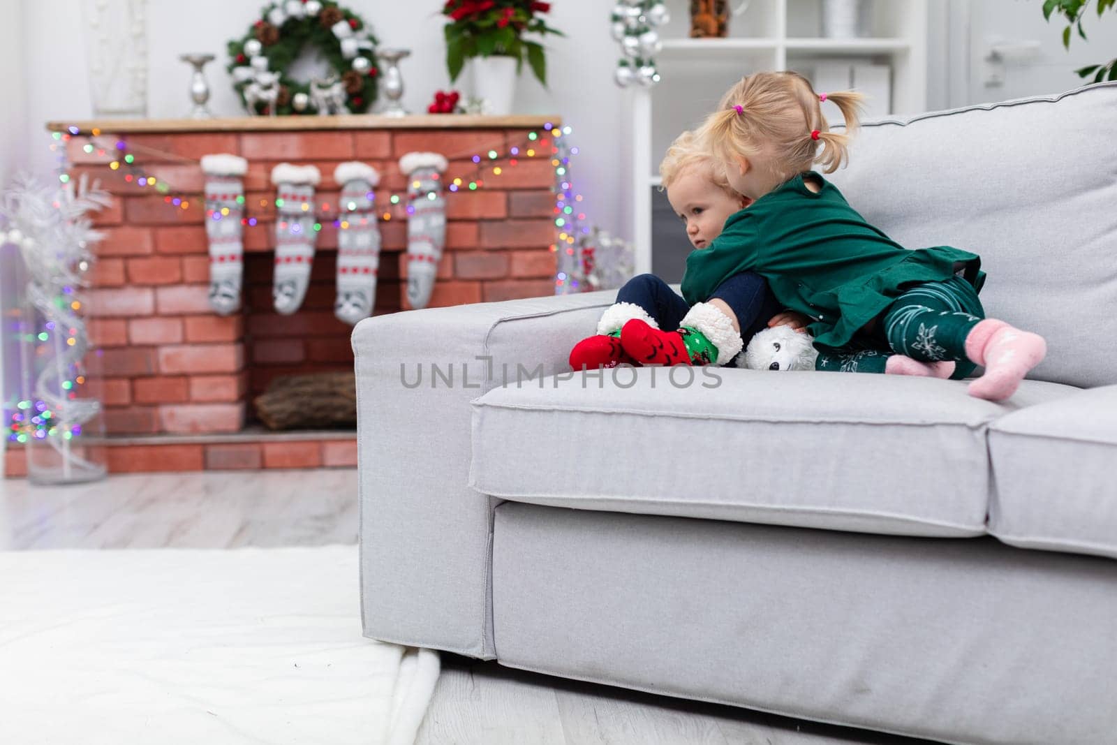 A gray couch stands in a room near a brick fireplace. On the couch sit two small children: a boy and a girl. The sister hugs her brother tightly embracing him joyfully.
