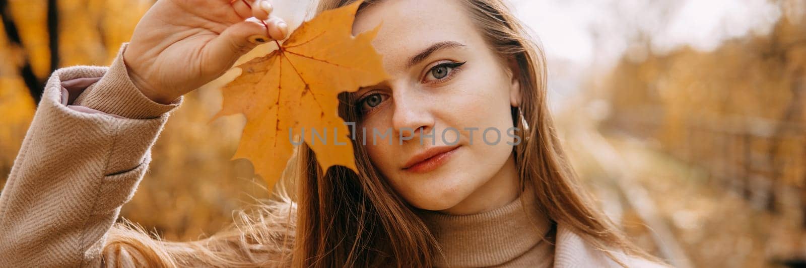 Portrait of a woman with an autumn maple leaf. Railway, autumn leaves, a young long-haired woman in a light coat coat, close-up. by Annu1tochka