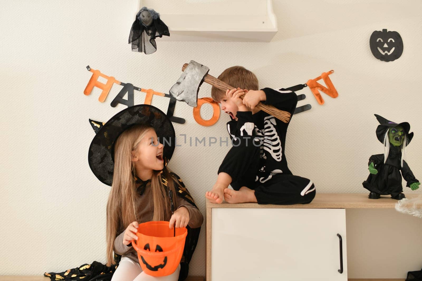 Children in skeleton and witch costume laughing at home halloween