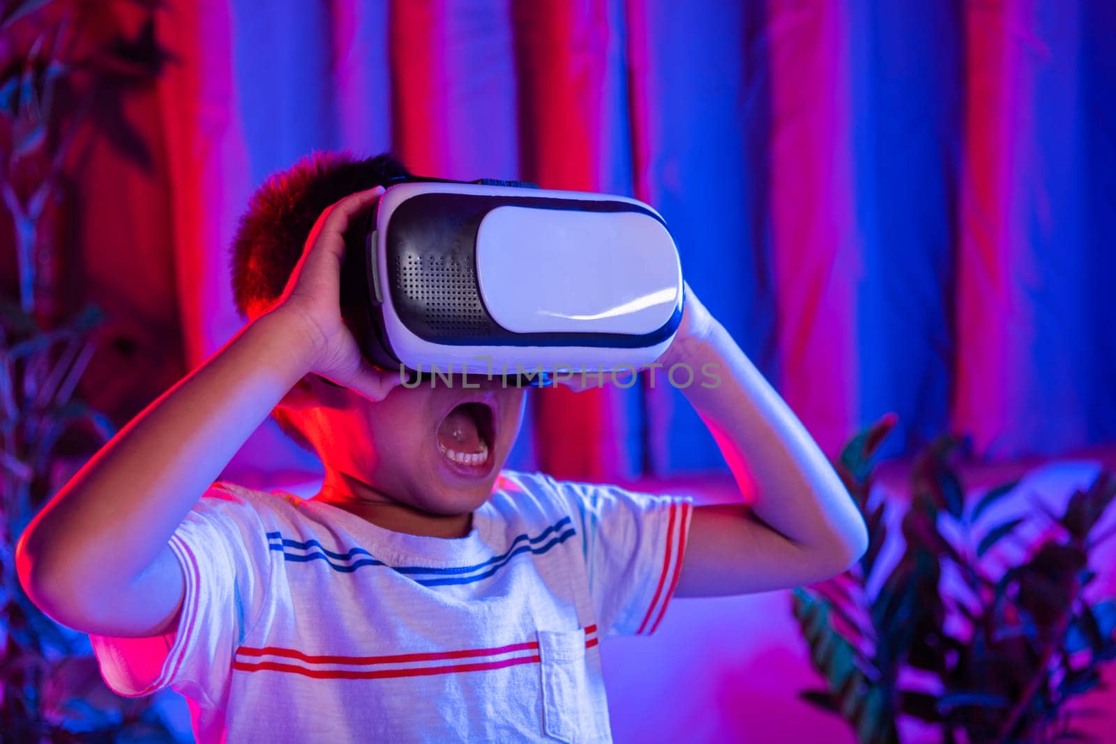 Asian little kid boy wearing virtual reality goggles experiencing reality, Child wear VR helmet excited open mouth at home dark purple and blue background, Virtual technology