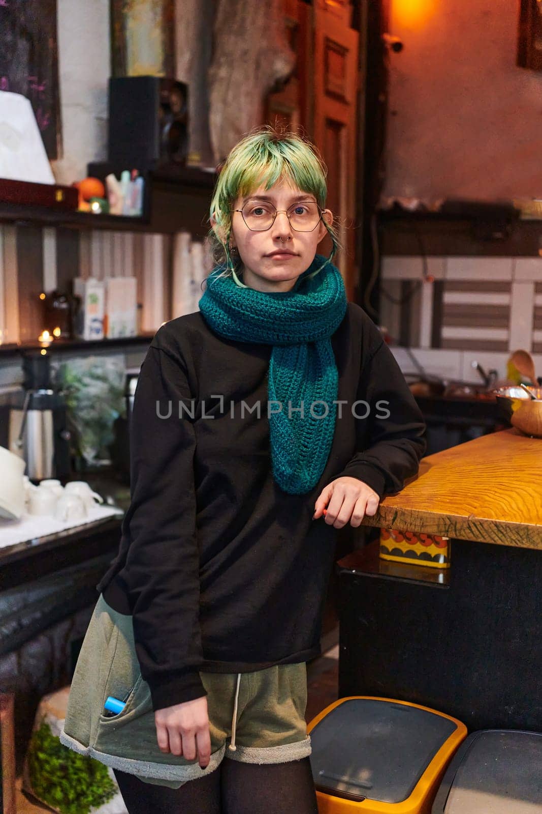 A modern and intriguing girl with striking blue hair enjoys a night out in a cafe transformed into a passionate Halloween-style setting, exuding a captivating and witchy ambiance.