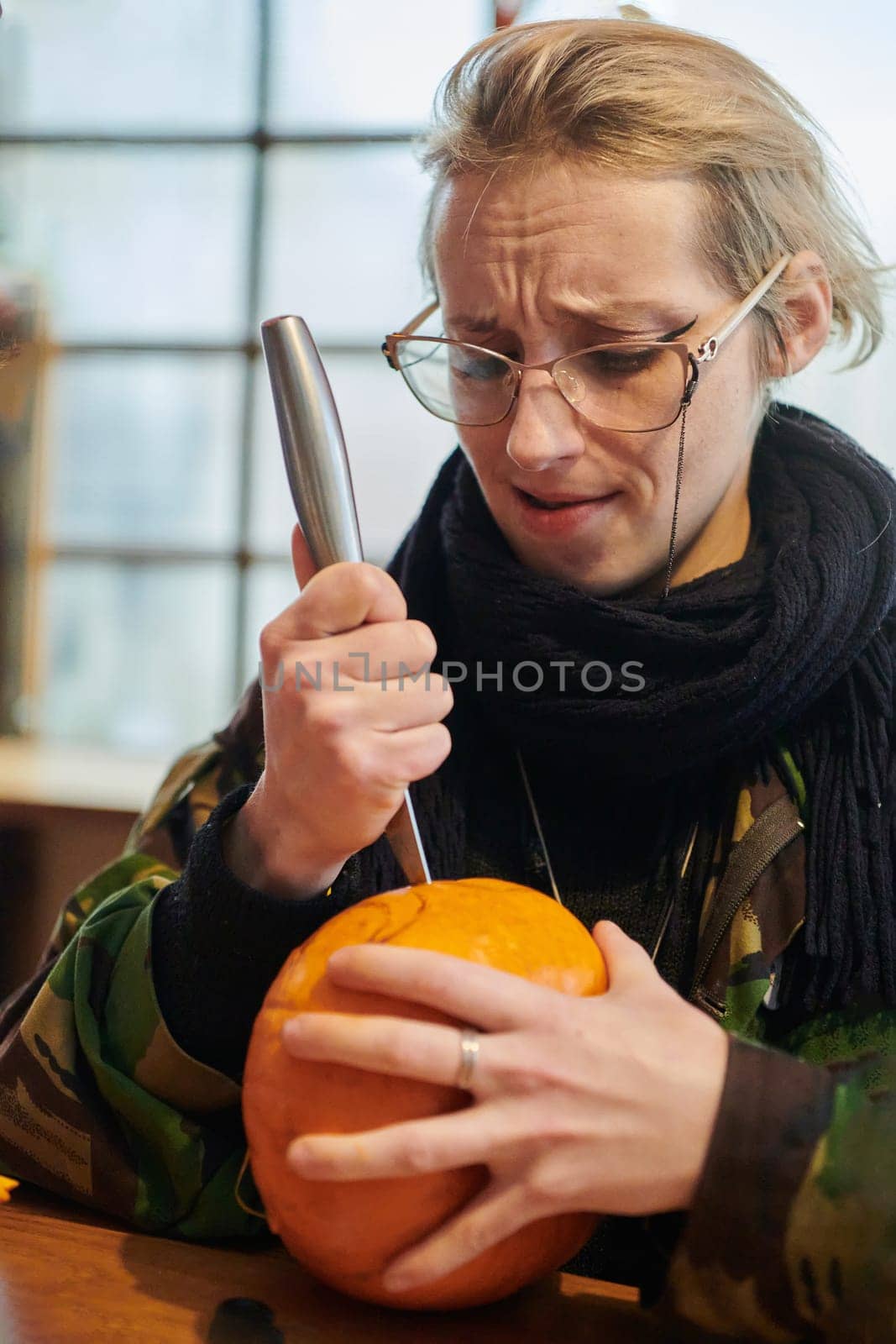 A modern blonde woman in military uniform is carving spooky pumpkins with a knife for Halloween night.