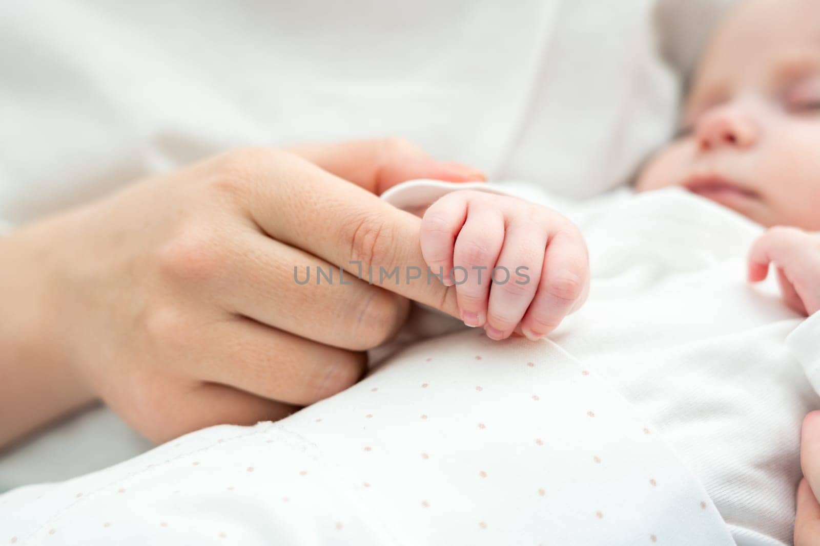 Close-up showcases the sleeping newborn baby holding onto mother's hand, manifesting innate bond and protection