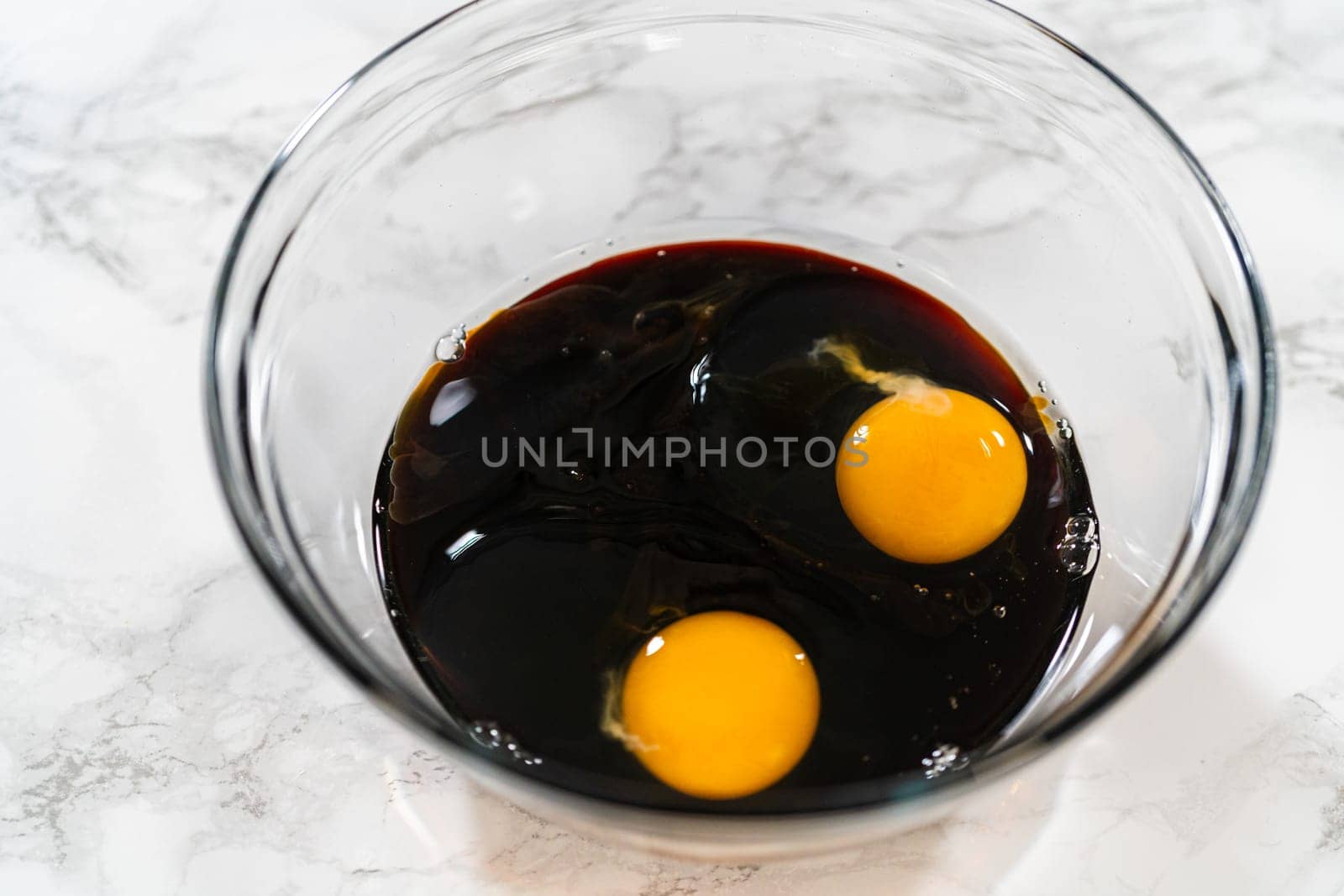 A top-down view of dark molasses and two eggs in a glass bowl, part of the wet ingredients for Zesty Orange Gingerbread Cookie Dough. The molasses adds depth and a rich color to the gingerbread.