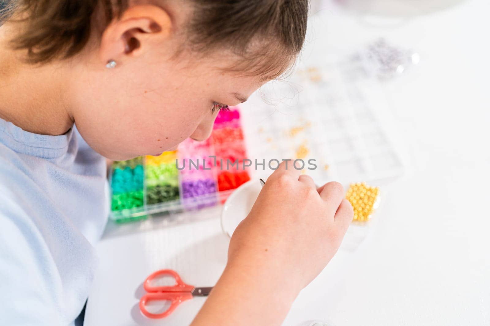 Little girl enjoys crafting colorful bracelets with vibrant clay beads set.