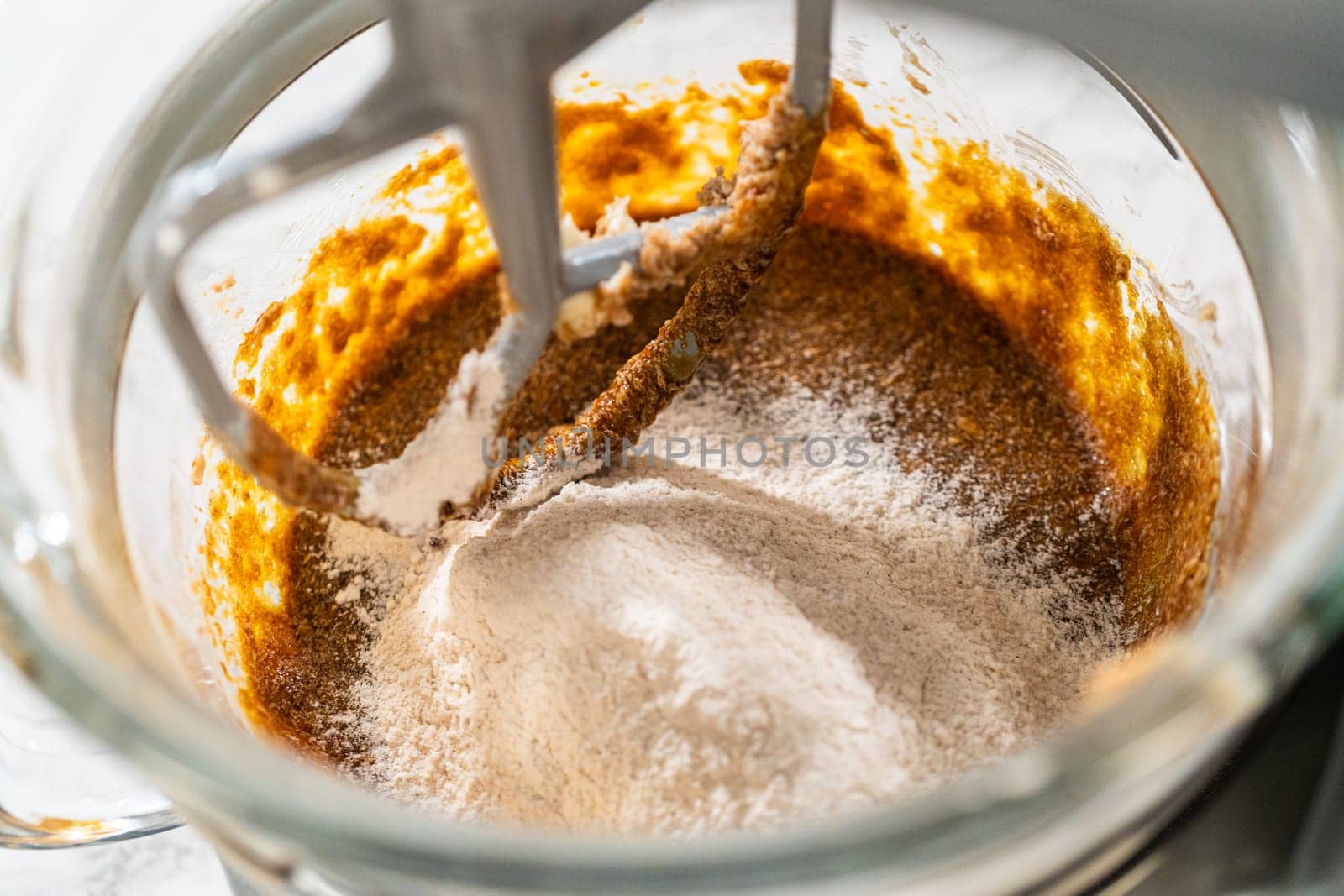 Dry ingredients gradually added to the wet mixture in the stand mixer for Zesty Orange Gingerbread Cookie Dough. Flour and spices are incorporated for a balanced, spiced dough texture.
