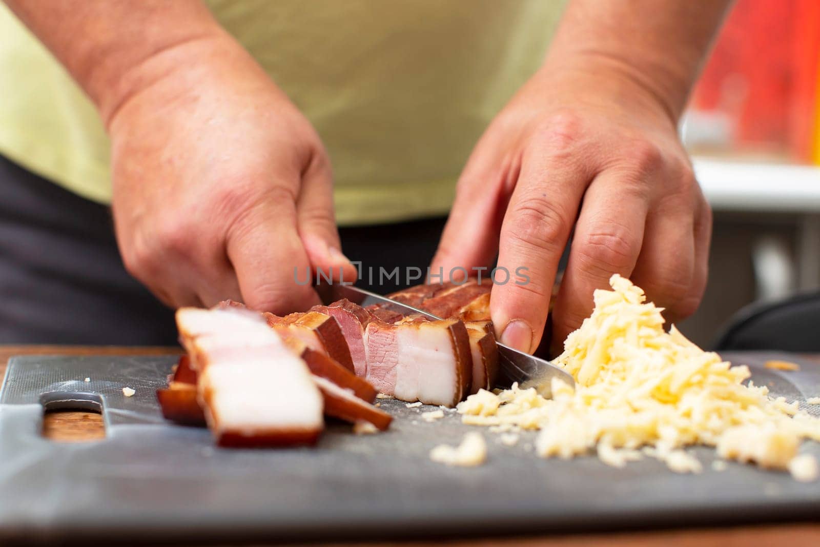 Man's hands cut a piece of pork bacon.