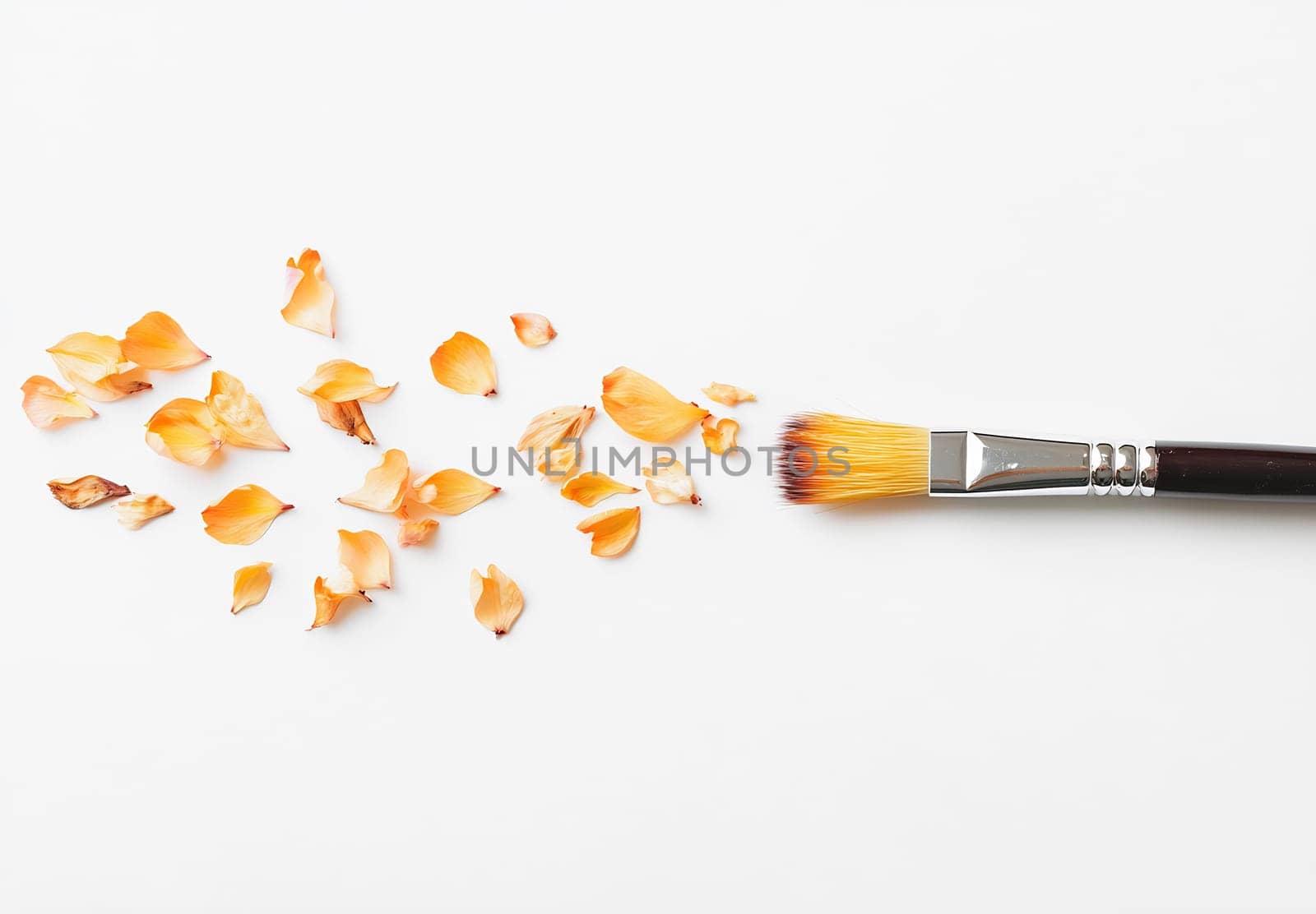 A brush lies next to scattered dried orange petals on a white backdrop, showcasing a creative workspace or craft activity.