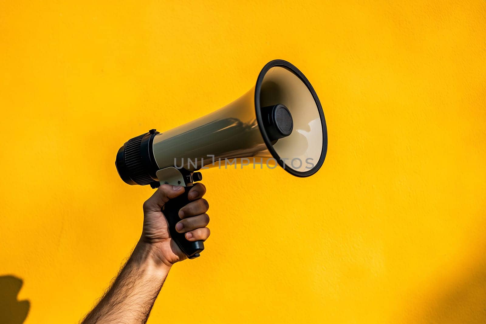 A hand is raised, gripping a megaphone against a vibrant yellow backdrop, ready to amplify a message or call for attention.