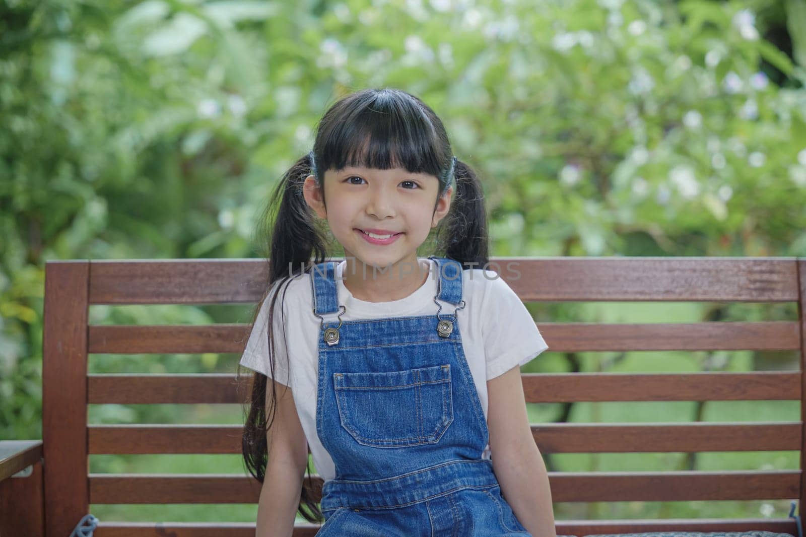 Asian young attractive girl seated on wooden bench in the garden scenic outdoor setting, Kid sitting on the bench in nature park