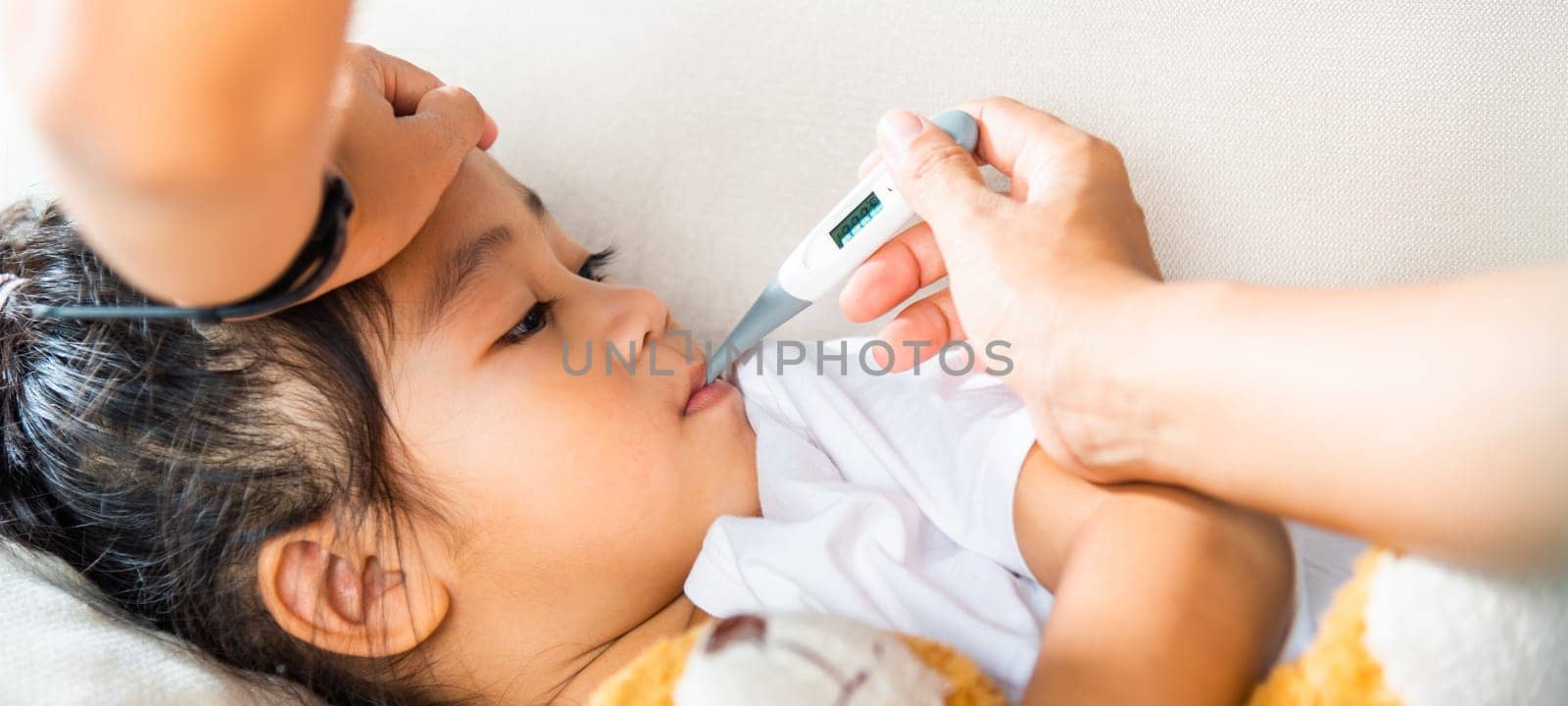 Sick kid. Mother parent checking temperature of her sick daughter with digital thermometer in mouth, child laying in bed taking measuring her temperature for fever and illness, healthcare