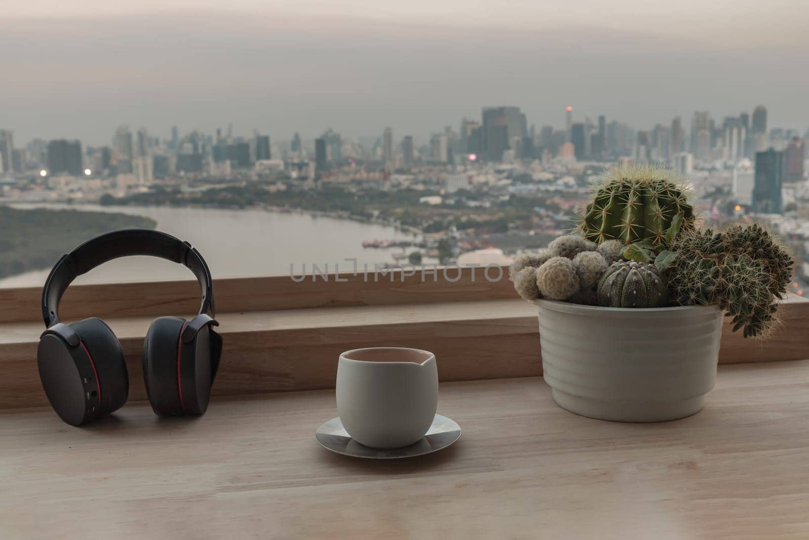Bangkok, Thailand 02 Jan,2025 - Relaxation area or Working space in Condominium balcony overlooking river view. Ear headphones, Tea cup and Cactus pot on Wooden table, use it as your Wallpaper, Poster and Copy space, Selective focus.