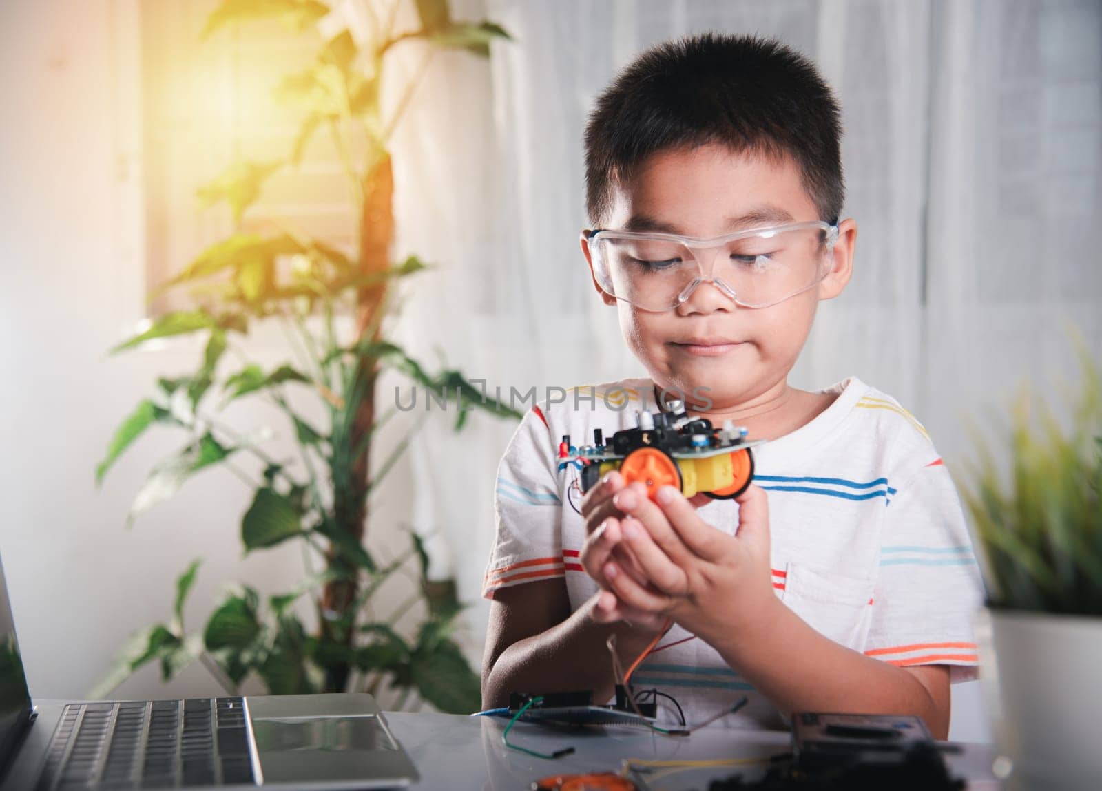 Little child trying assemble build wheel to car toy, Asian kid boy assembling wheel into Arduino robot car homework, creating electronic AI technology workshop online school lesson