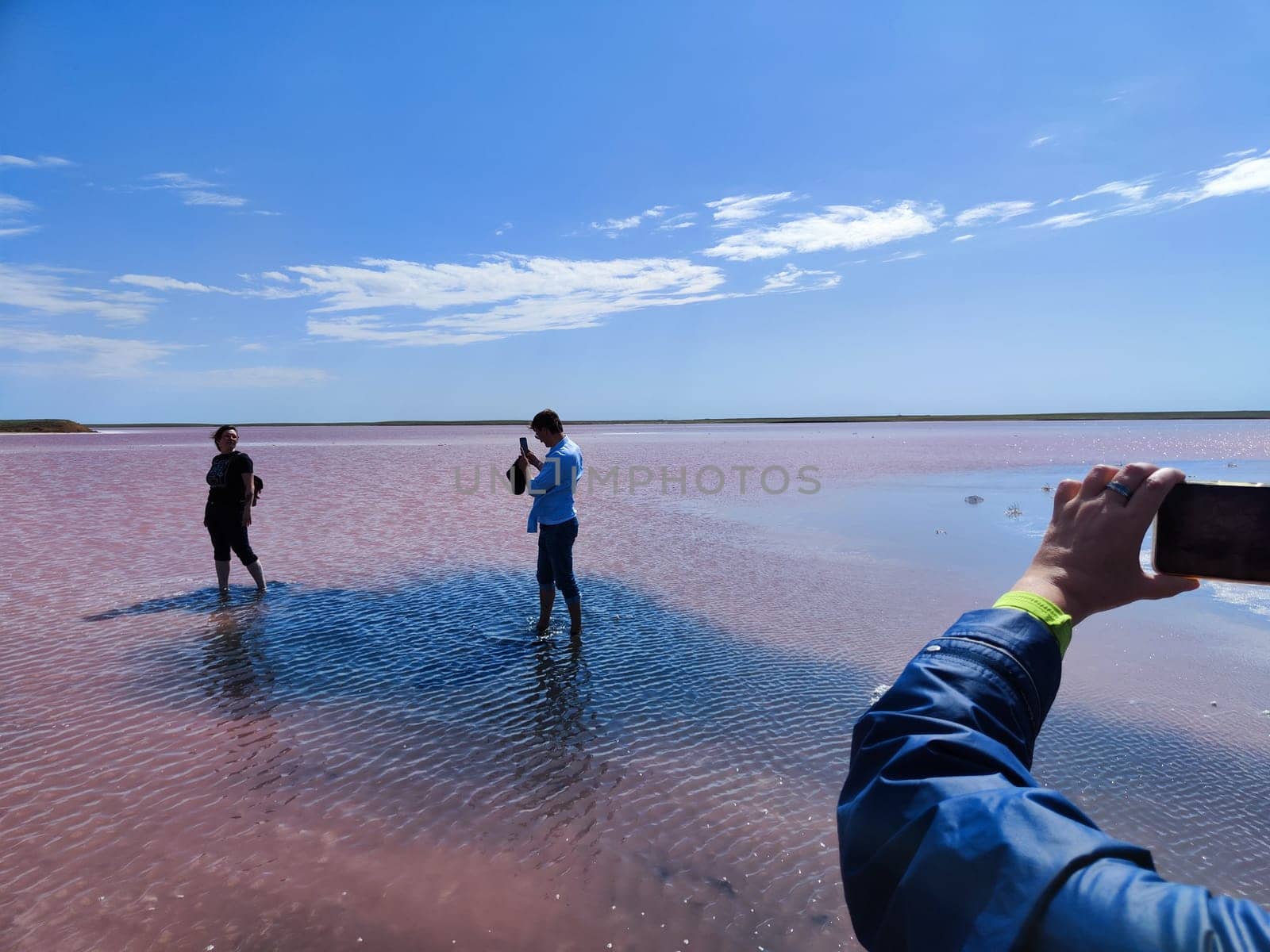 Elista, Russia - April 22, 2024: Visitors enjoy the stunning Pink Salt Lake in Kalmykia, Russia, capturing memories under clear blue skies with water reflecting the vibrant hues.