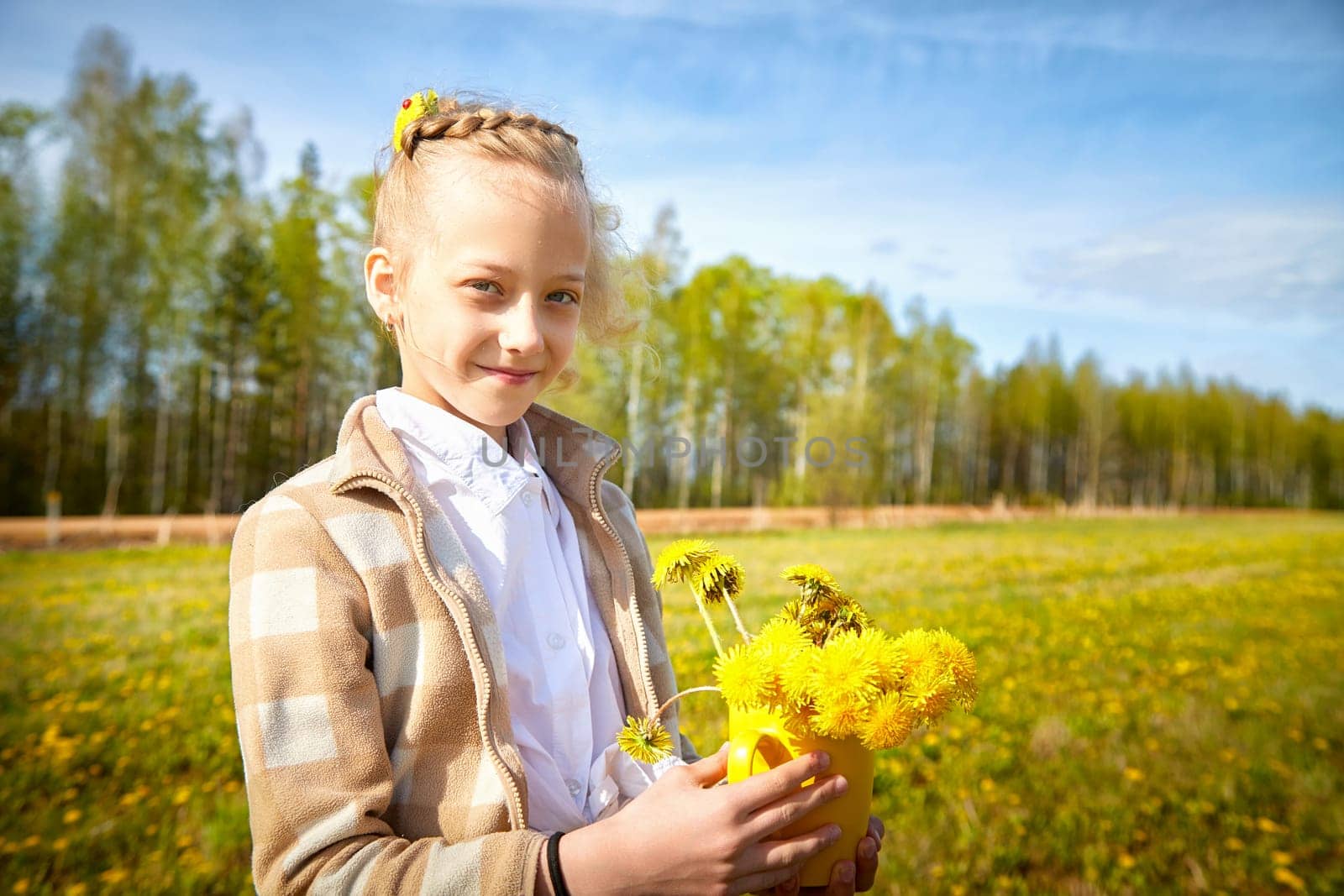 A cheerful girl carries a vibrant bouquet of dandelions amidst a beautiful green landscape filled with wildflowers under a clear sky.