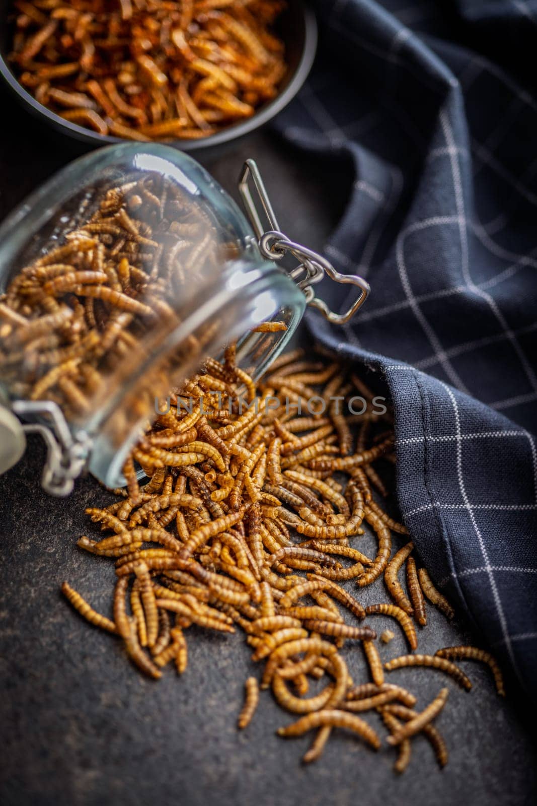 Dried salted worms. Roasted mealworms in jar on a black table.
