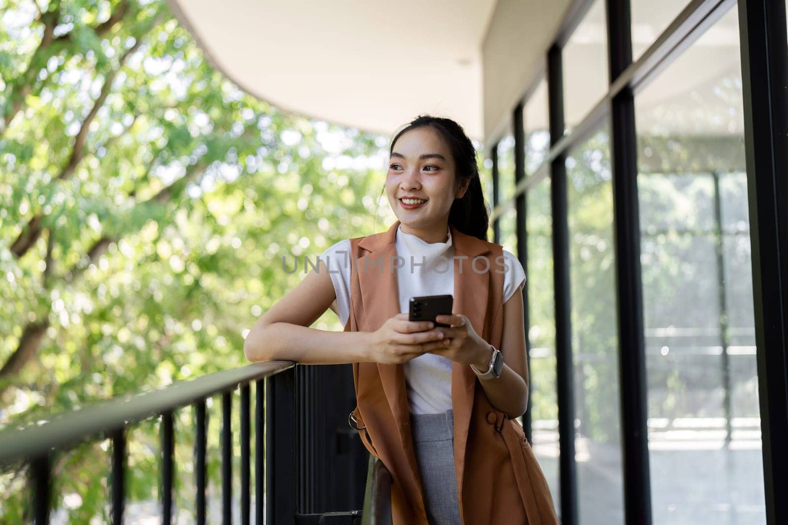 A cheerful woman enjoys her smartphone while relaxing on a balcony embodying a modern lifestyle amidst nature.