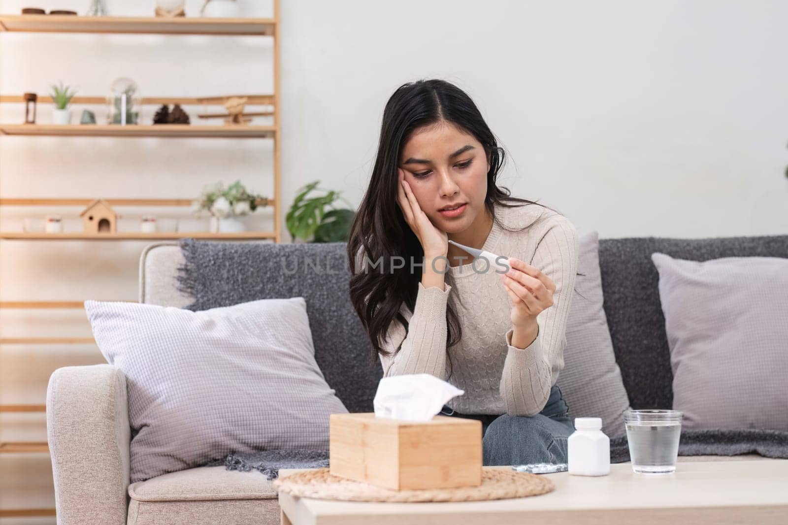 A woman at home feels sick and unwell while checking her temperature reflecting the struggle of managing health.
